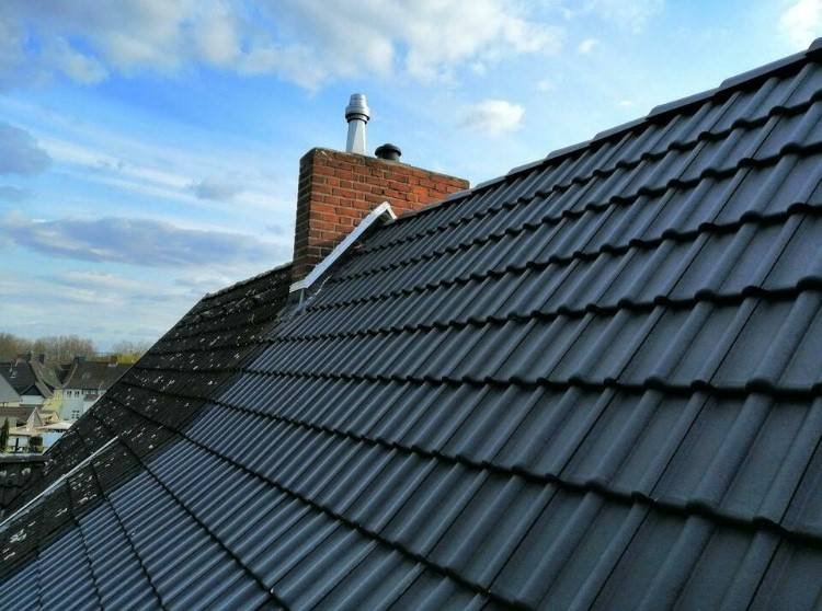 Frisch eingedecktes Steildach mit anthrazitfarbenen Ziegeln und Backstein-Schornstein vor blauem Himmel