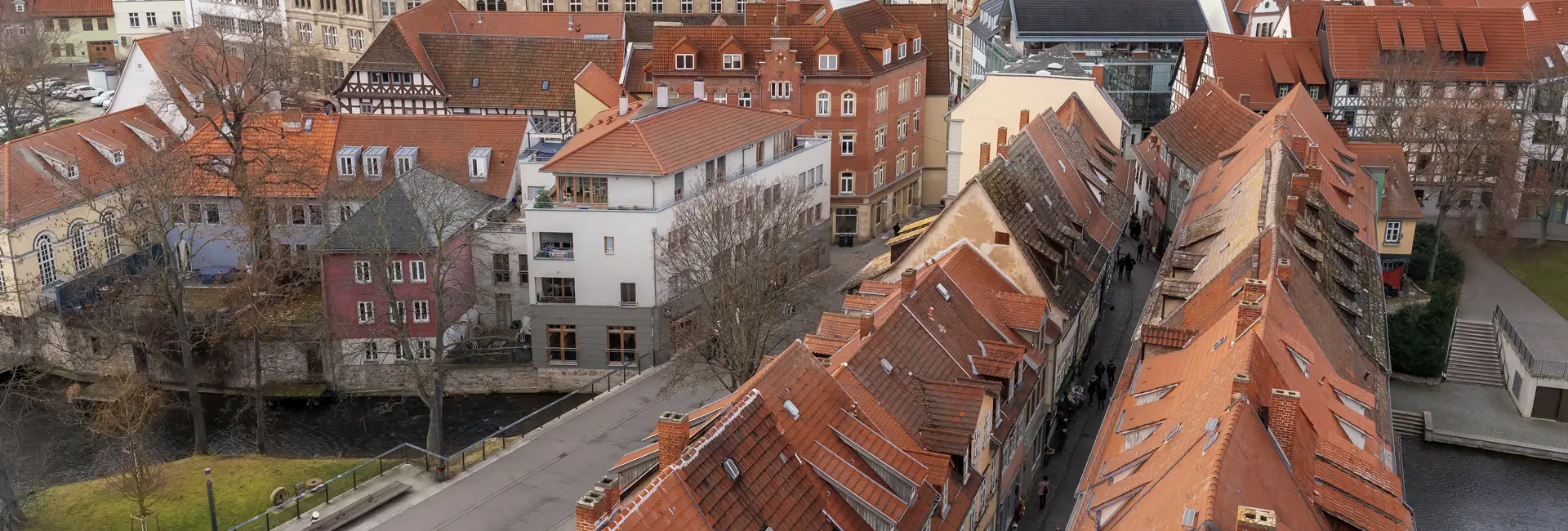 Luftaufnahme einer historischen europäischen Stadt mit roten Ziegeldächern, engen Gassen und einem Fluss, der daran entlangfließt.