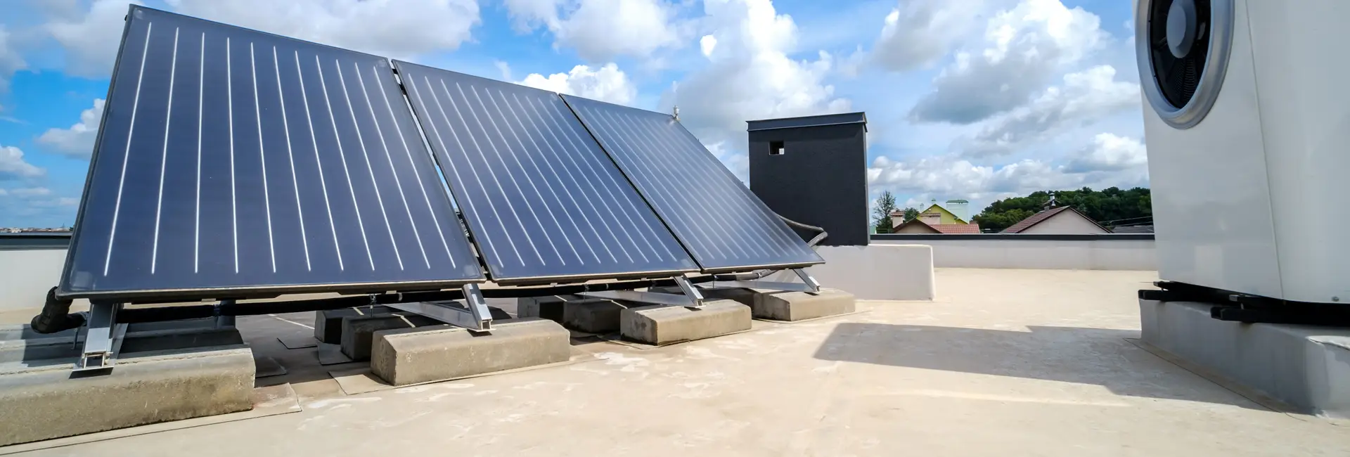 Auf einem Flachdach installierte Solarmodule mit Blick auf eine ferne Landschaft und einen bewölkten Himmel.